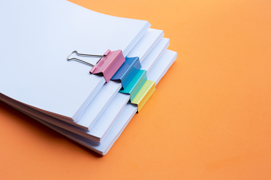 Stacking of business document with colorful binder clips on orange background.